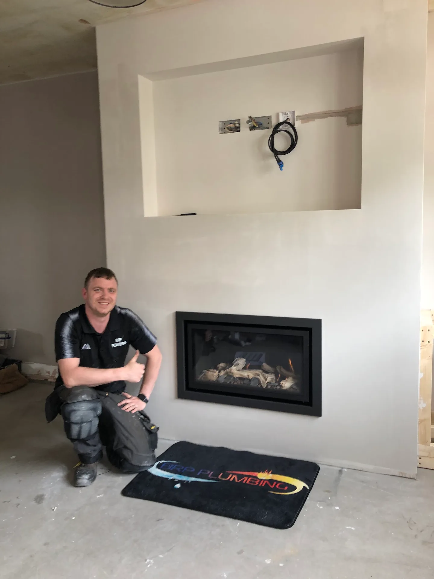 A BRP Plumbing team member beside a completed gas fire and branded protective mat