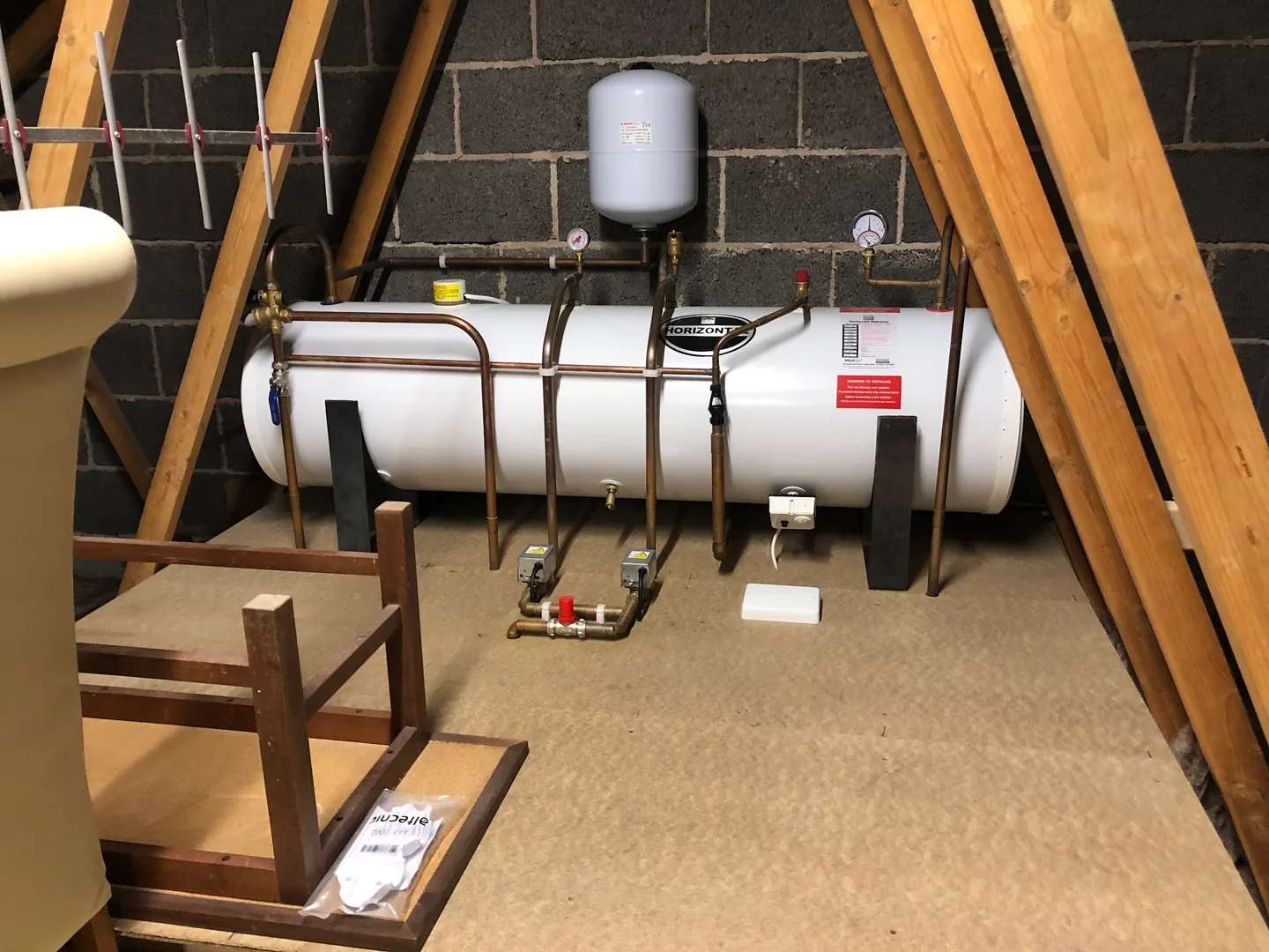 Horizontal hot water cylinder installed in a loft with copper pipework