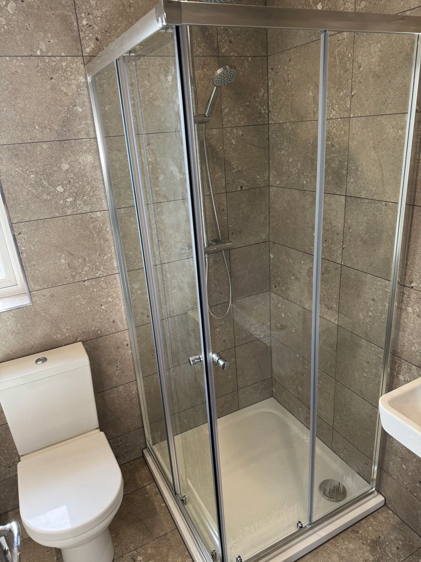 A completed glass shower enclosure with tiled walls and bathroom fittings